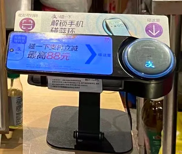 Alipay checkout terminal on a shop counter in China: on the left a scanning area labelled 此处可扫码, on the right a round pad with the Alipay logo for 碰一下