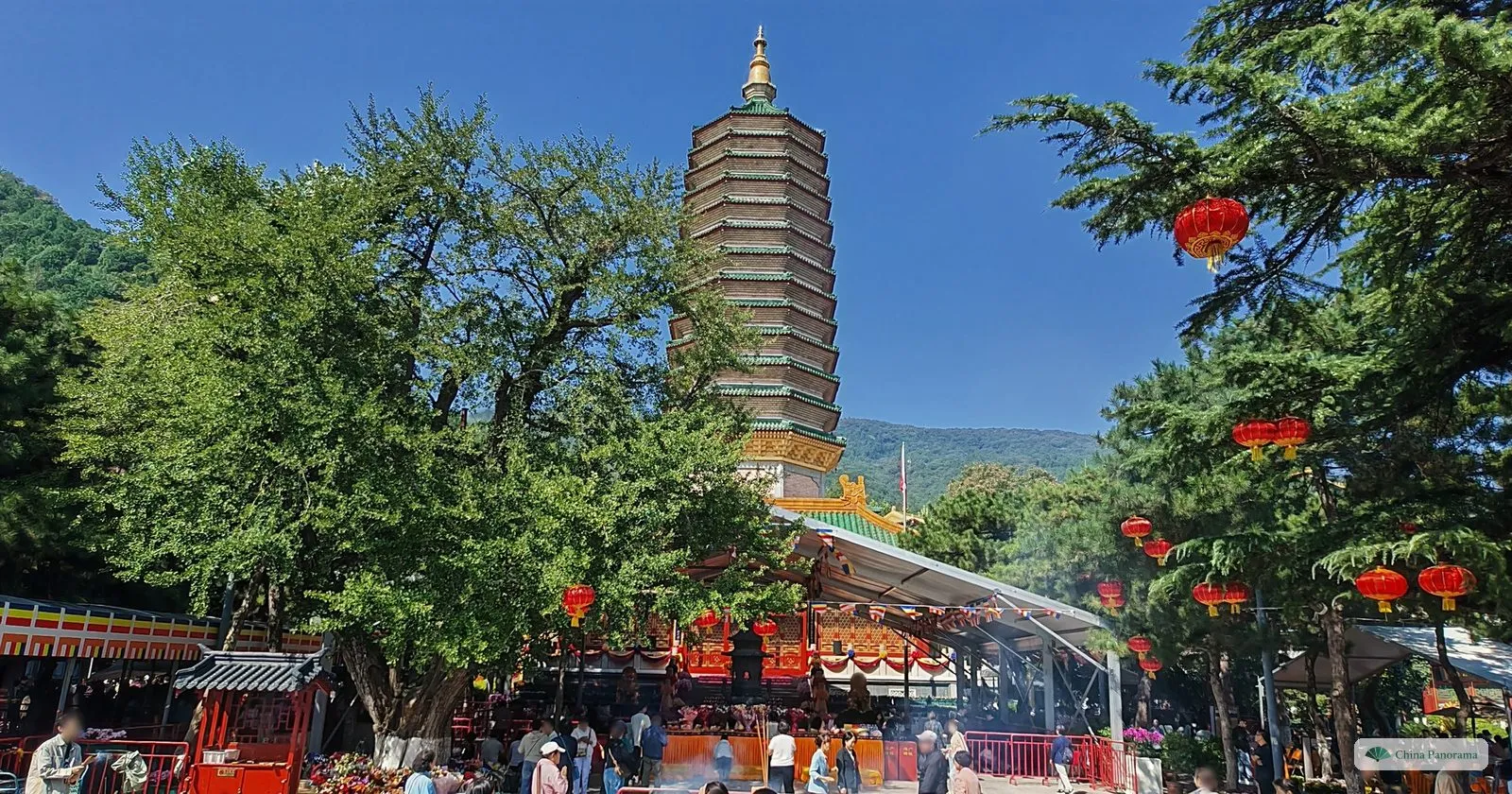 The tall pagoda of Lingguang Temple at Badachu rising above trees hung with red lanterns, with worshippers in the courtyard