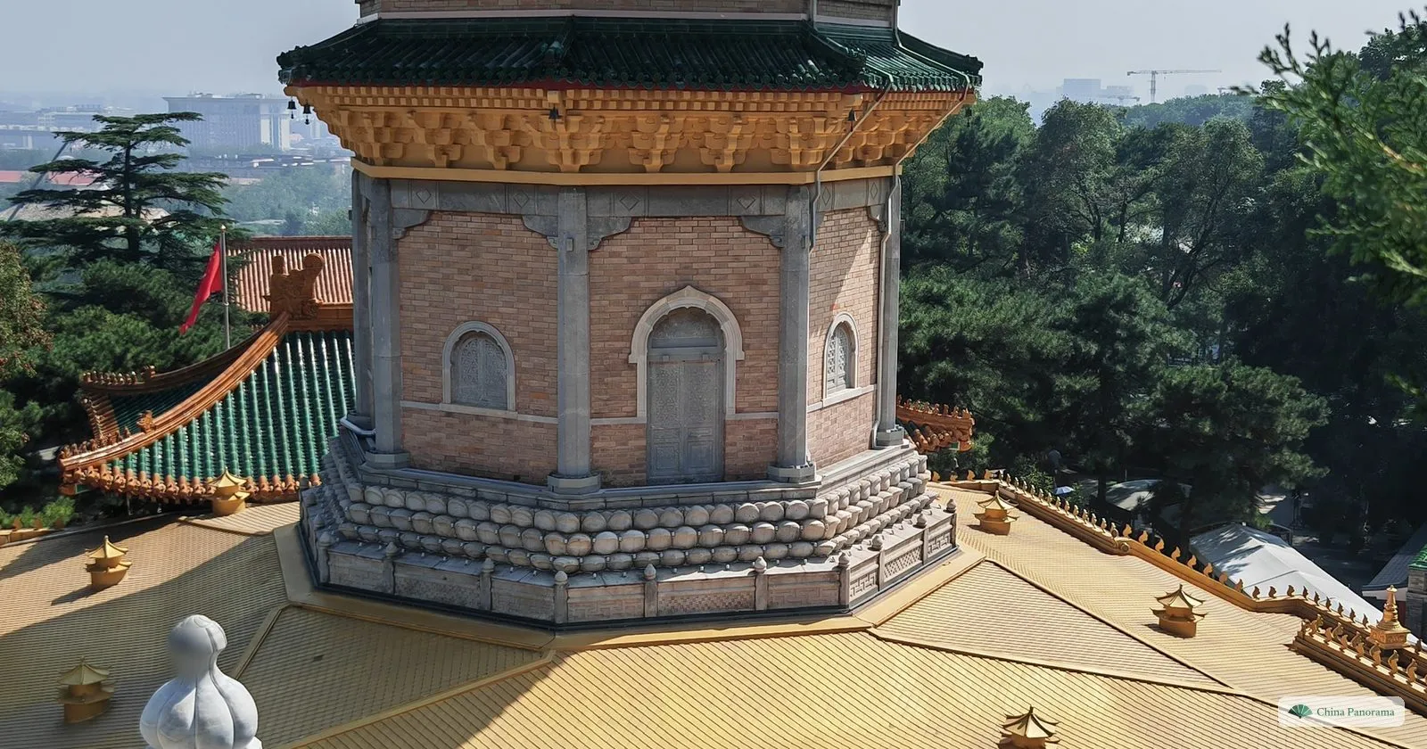 The brick and stone base of the pagoda at Lingguang Temple seen from above, with green-roofed halls and the city in the haze beyond