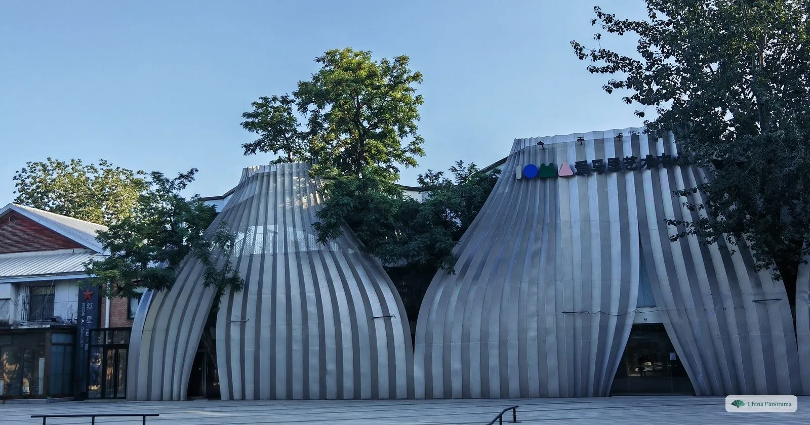 Two bulbous ribbed metal pavilions in front of a saw-tooth factory roof in the 798 Art District