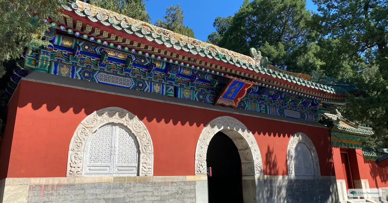 A red-walled gatehouse in Beihai Park with three arched doorways framed in carved white marble and a roof of green and yellow glazed tiles