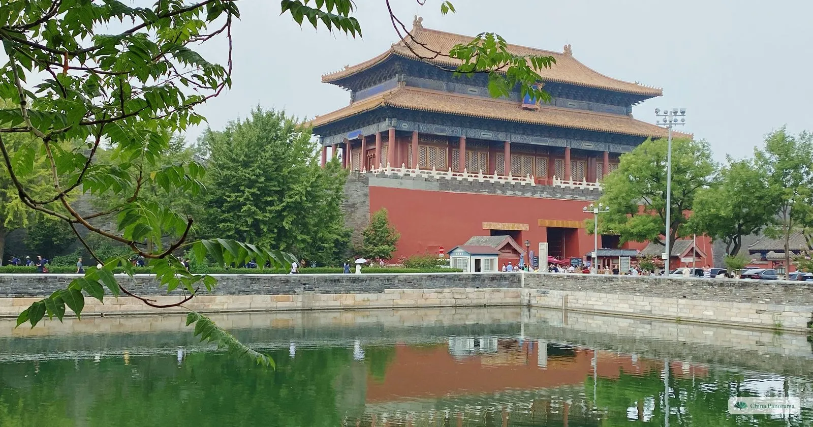 A gate tower of the Forbidden City with a double yellow-tiled roof on a red base, reflected in the green water of the palace moat