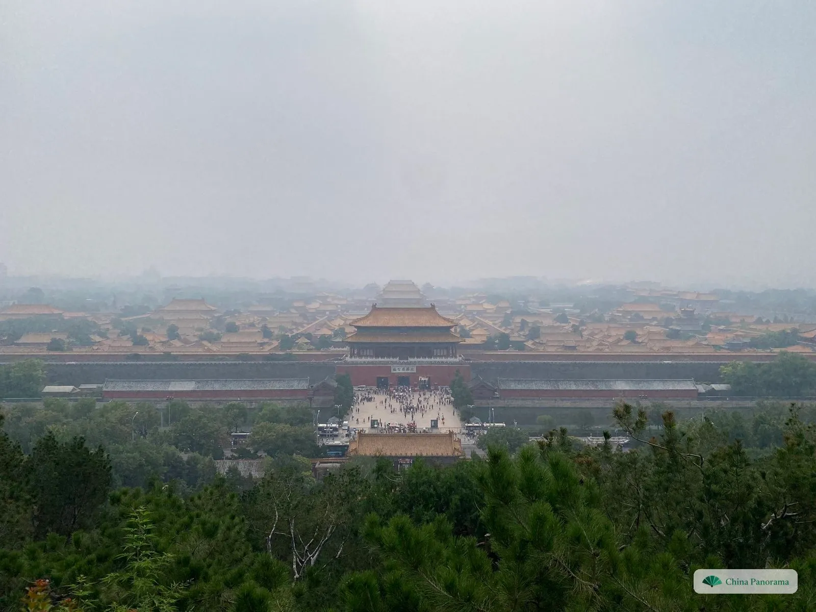 The Forbidden City seen from the top of Jingshan on a hazy day: the north gate in the centre and yellow roofs stretching away on both sides, above the pines of the park