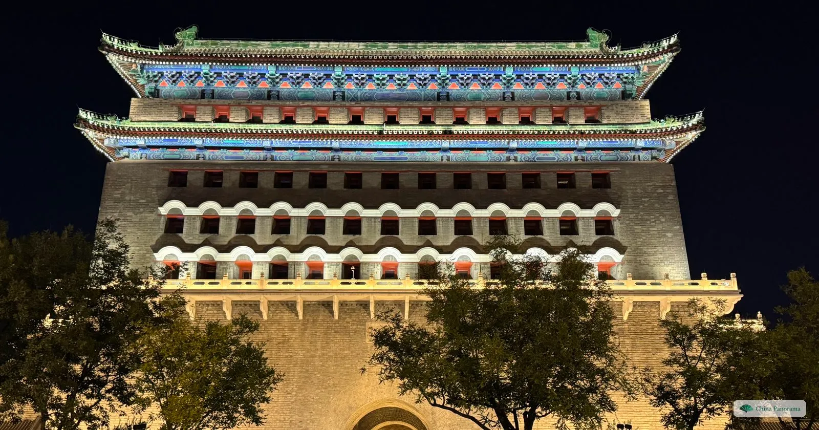 The Zhengyangmen archery tower at Qianmen floodlit at night, with rows of arrow slits in its grey brick wall and a green-tiled double roof