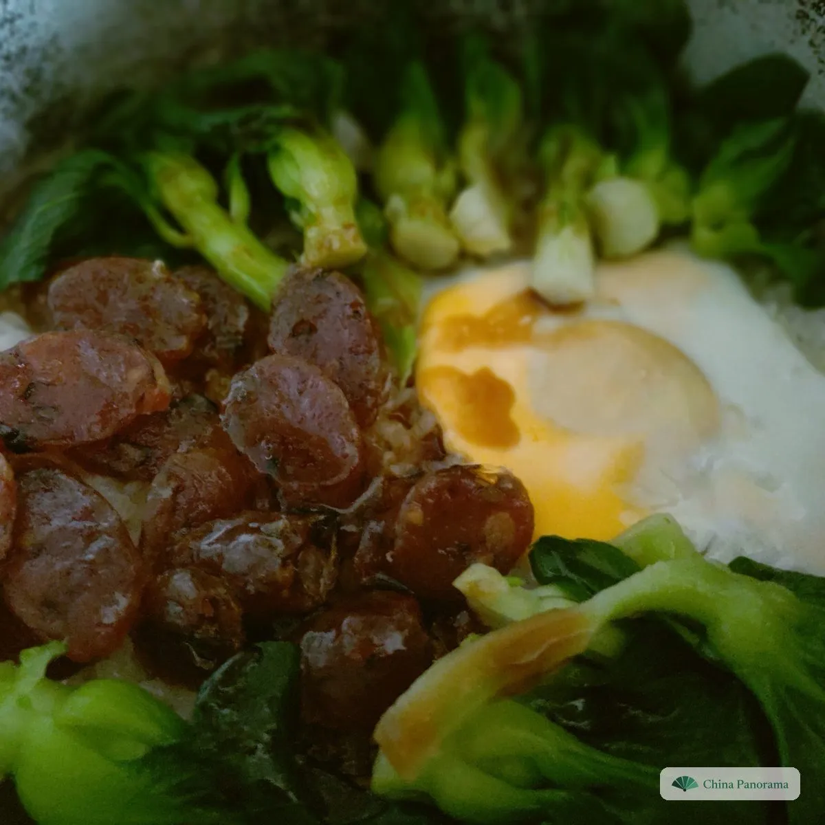 Rice in a dark clay pot under slices of Chinese sausage, a soft egg and bok choy