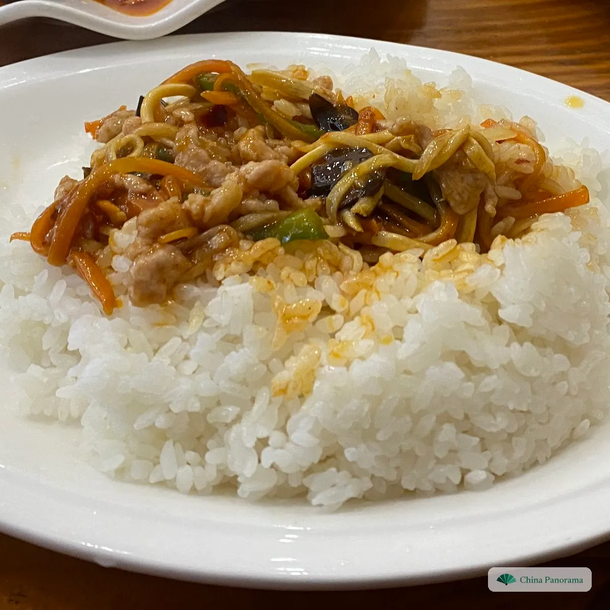 A mound of plain white rice on a plate, with shredded pork, wood ear and carrot in a glossy sauce spooned over one side