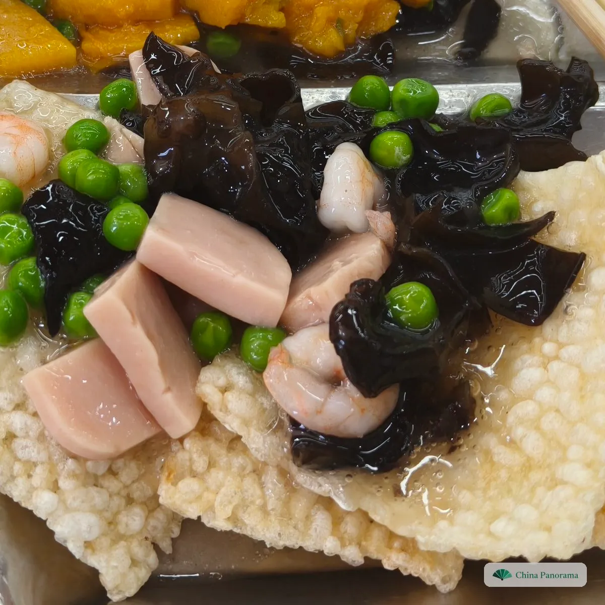 Puffed squares of crisp rice crust under a sauce with shrimp, squid, wood ear and green peas, on a steel tray