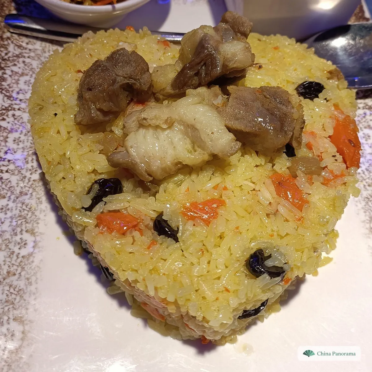 Yellow rice shaped into a heart, dotted with carrot and raisins, with chunks of lamb on top