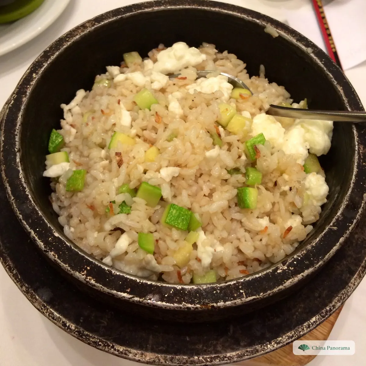 Pale fried rice with diced green courgette and white egg white in a black stone pot, a spoon in it