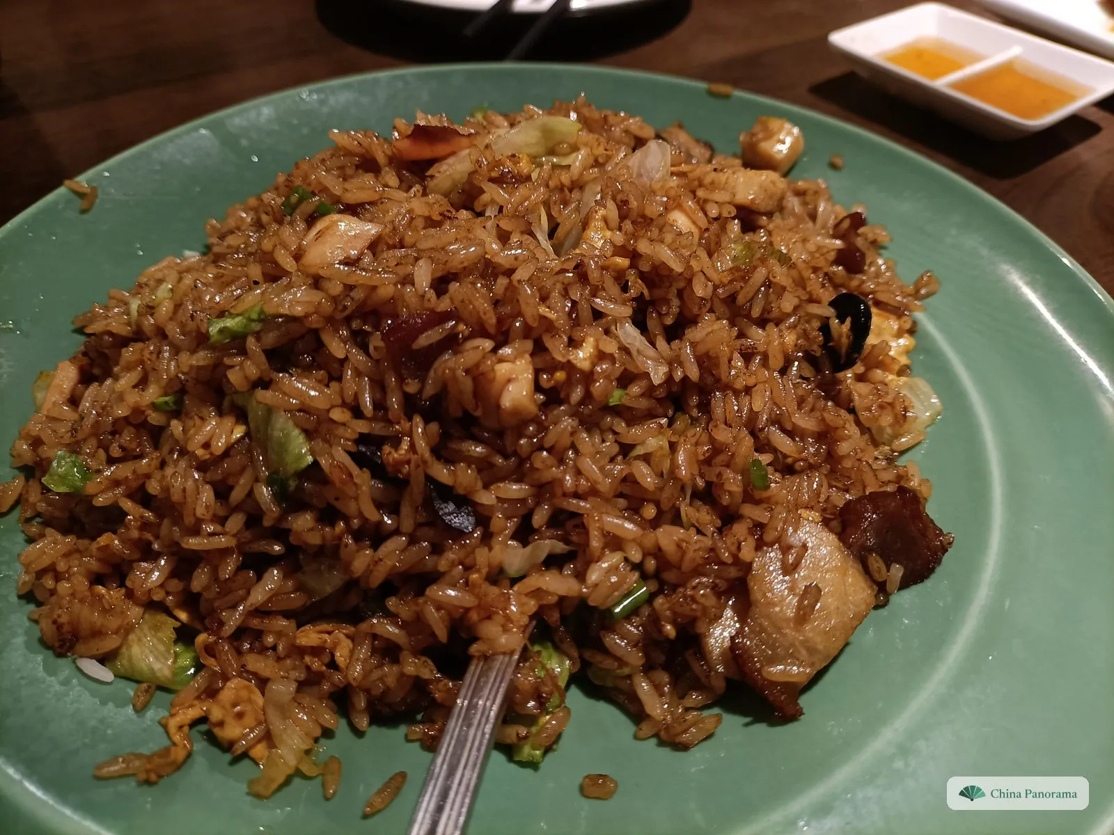 A heap of brown, glossy fried rice on a pale green plate, with pieces of cured pork, chicken and shredded lettuce; a fork stuck in it