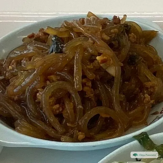A small oval dish of shiny brown glass noodles with minced pork