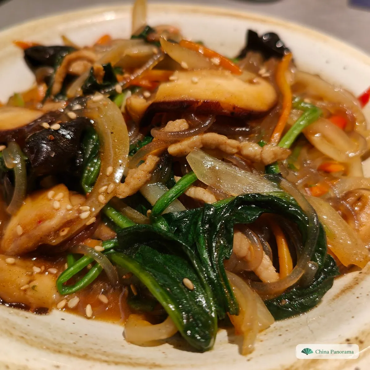 Glossy glass noodles stir-fried with shiitake, wood ear, spinach, onion, carrot and pork, sprinkled with sesame seeds