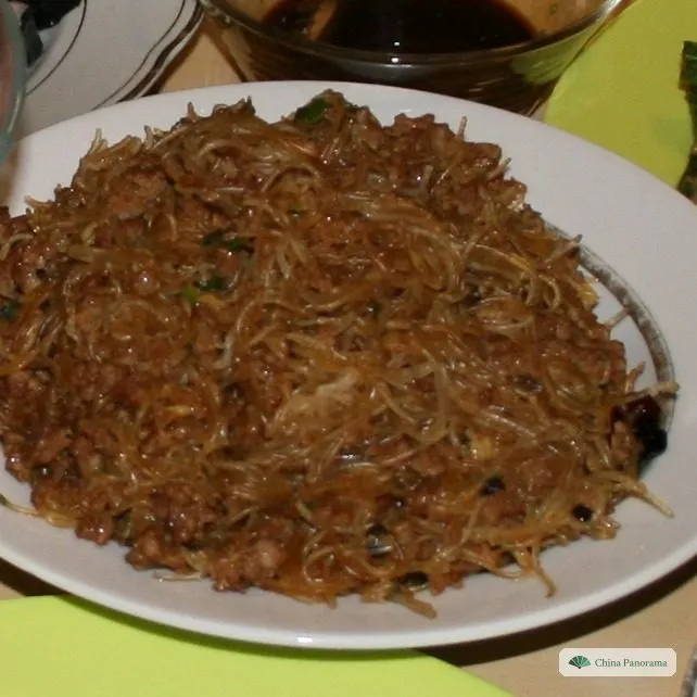 A white plate piled with thin, soy-brown rice noodles mixed with minced pork, other dishes at the edges
