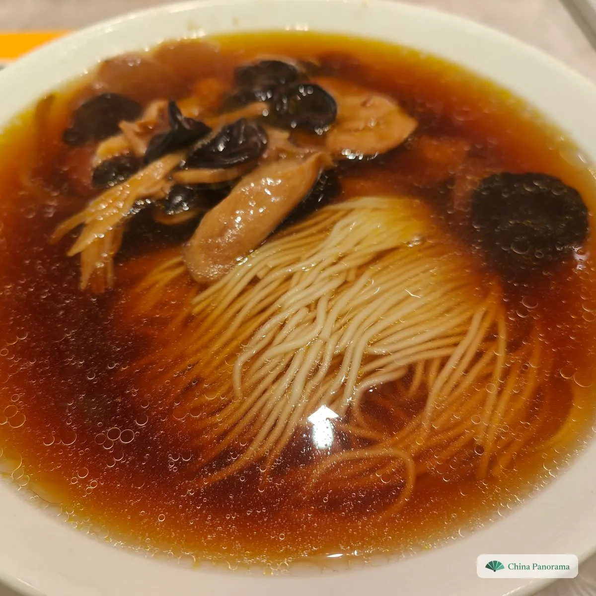 Thin noodles in a bowl of dark, clear broth, topped with shiitake mushrooms, wood ear and pieces of wheat gluten