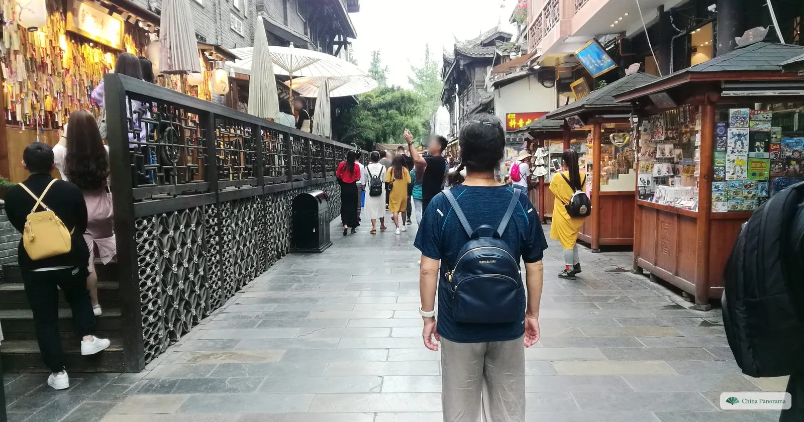 A paved lane with a carved brick screen on the left, wooden kiosks selling postcards and souvenirs on the right and a visitor with a backpack in the middle