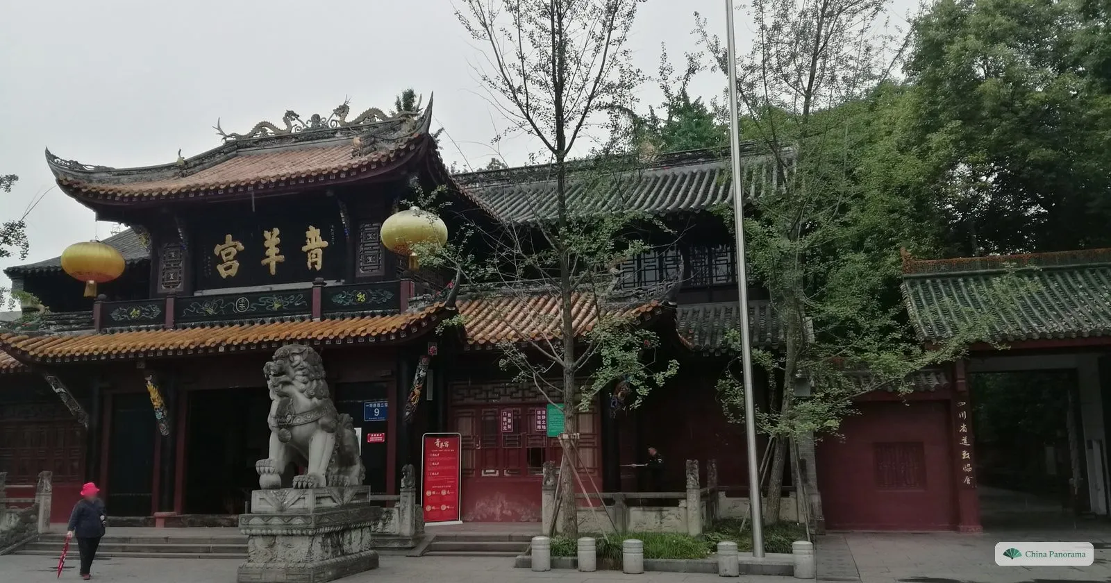 The gate of Qingyang Palace: a red building with upturned eaves, a black plaque 青羊宮 with gold characters, yellow lanterns and a stone lion in front