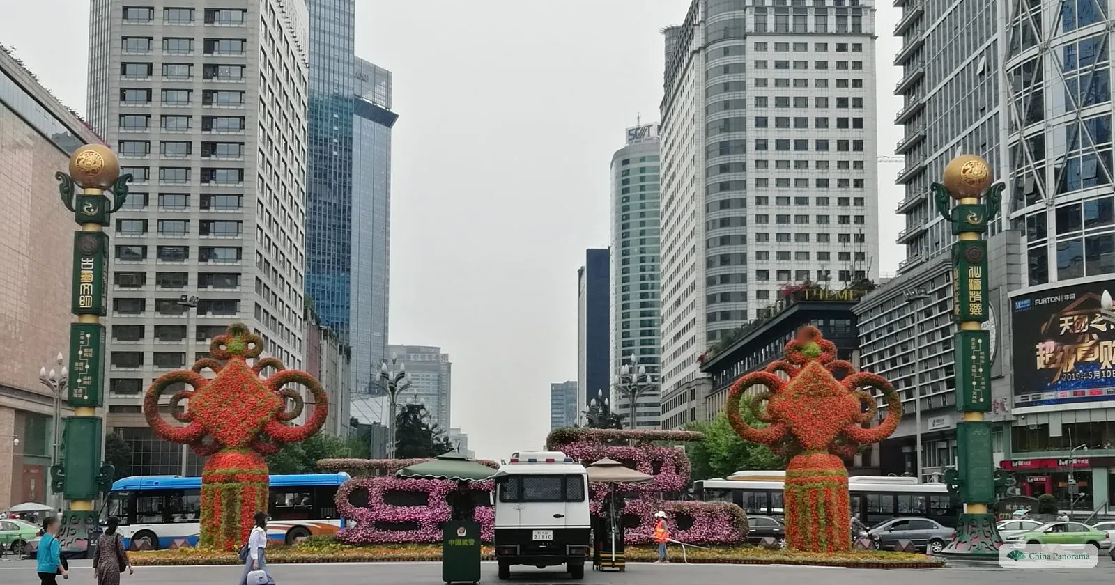 Looking south from Tianfu Square down a wide avenue between office towers, two tall green-and-gold columns and big flower displays shaped like Chinese knots