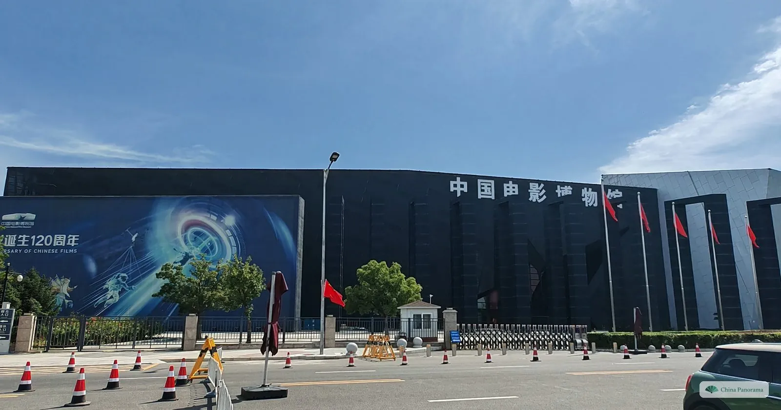 The black box-shaped building of the China National Film Museum with a large poster on its front, seen from the road