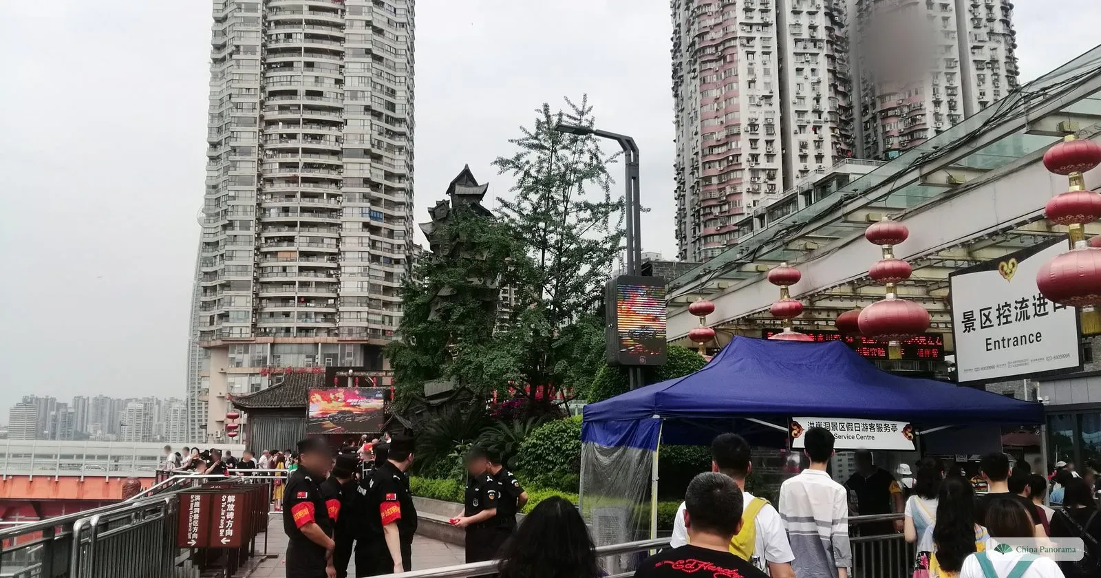 The crowd-control entrance at Hongyadong: uniformed security staff by a railing, a blue tent and a sign reading 景区控流进口 Entrance, with apartment towers behind