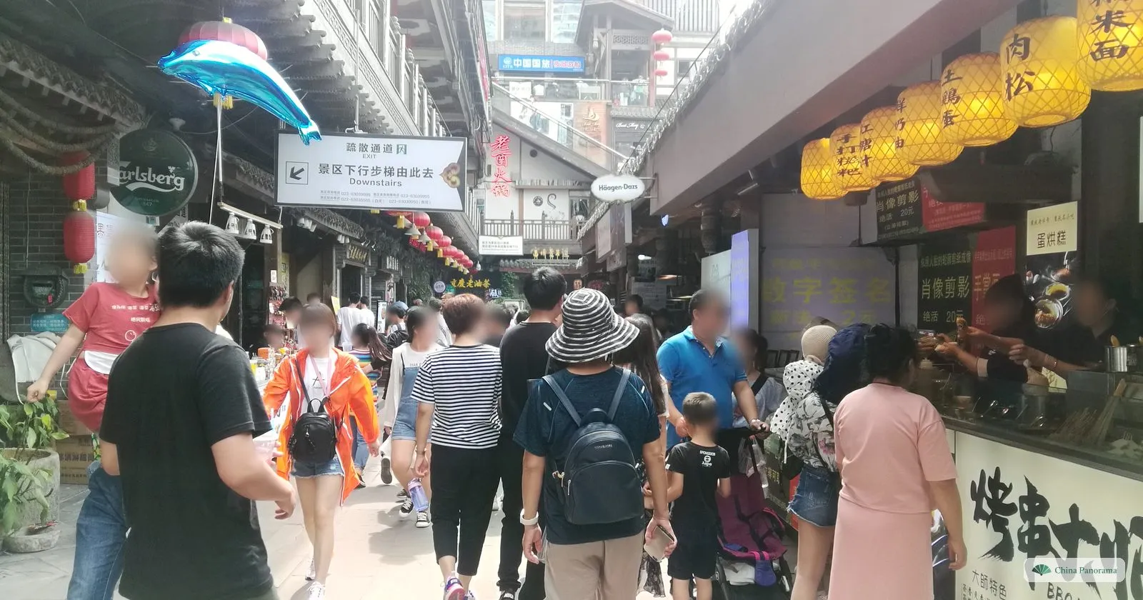 A crowded covered lane inside Hongyadong with snack stalls, yellow lanterns, a sign reading Downstairs and families walking through