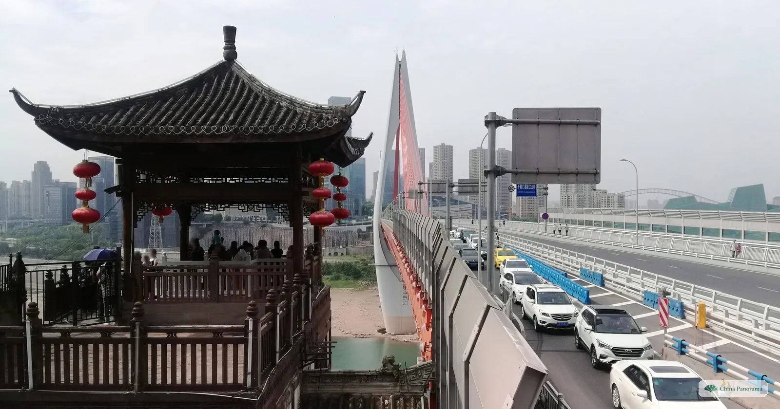 A wooden pavilion with red lanterns on a terrace above the Jialing, next to the approach road of the Qiansimen Bridge with its white tower and a queue of cars