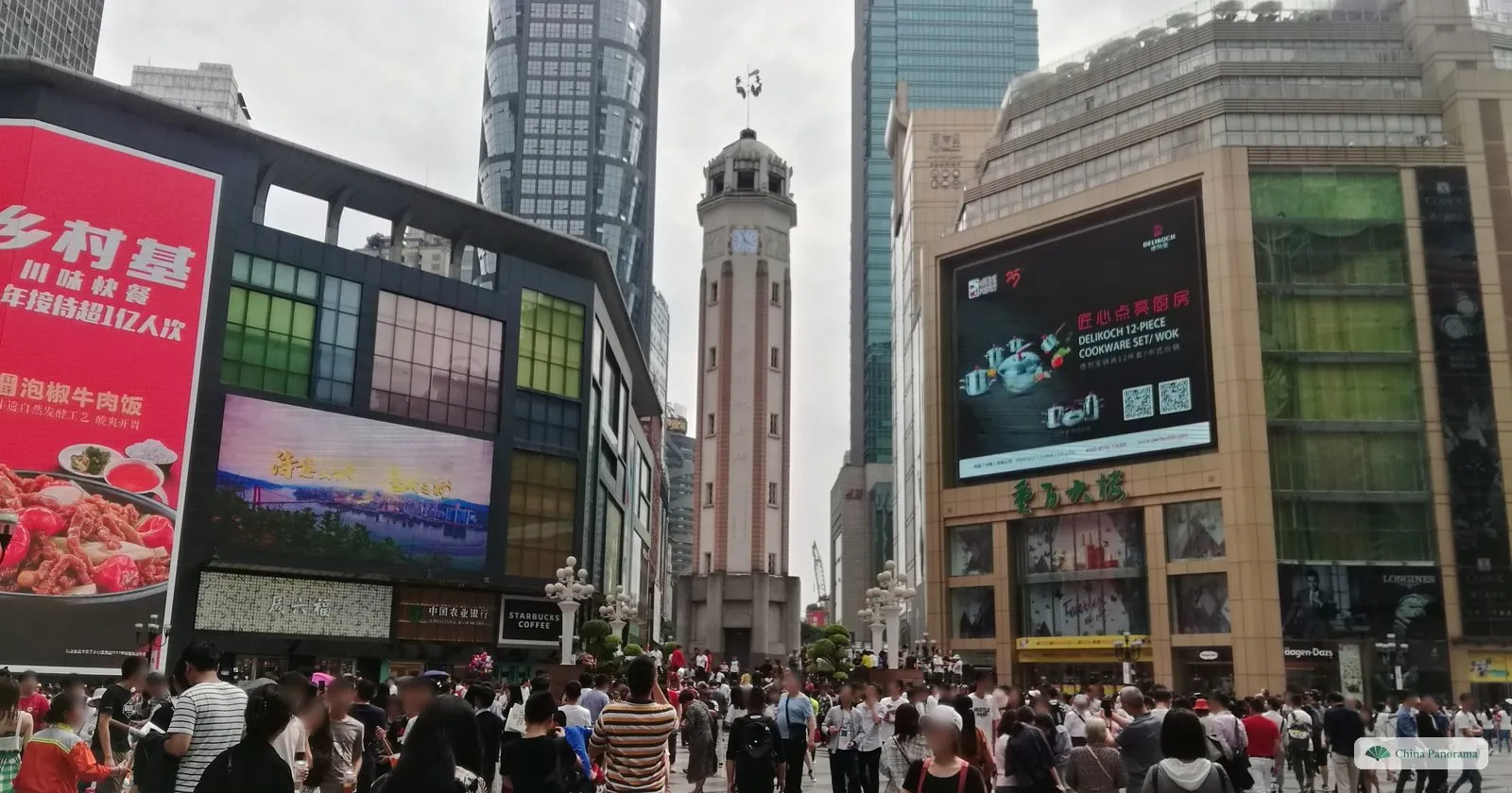 The tall, slim Jiefangbei monument with its clock between shopping centres with huge advertising screens, a dense crowd in the square in front