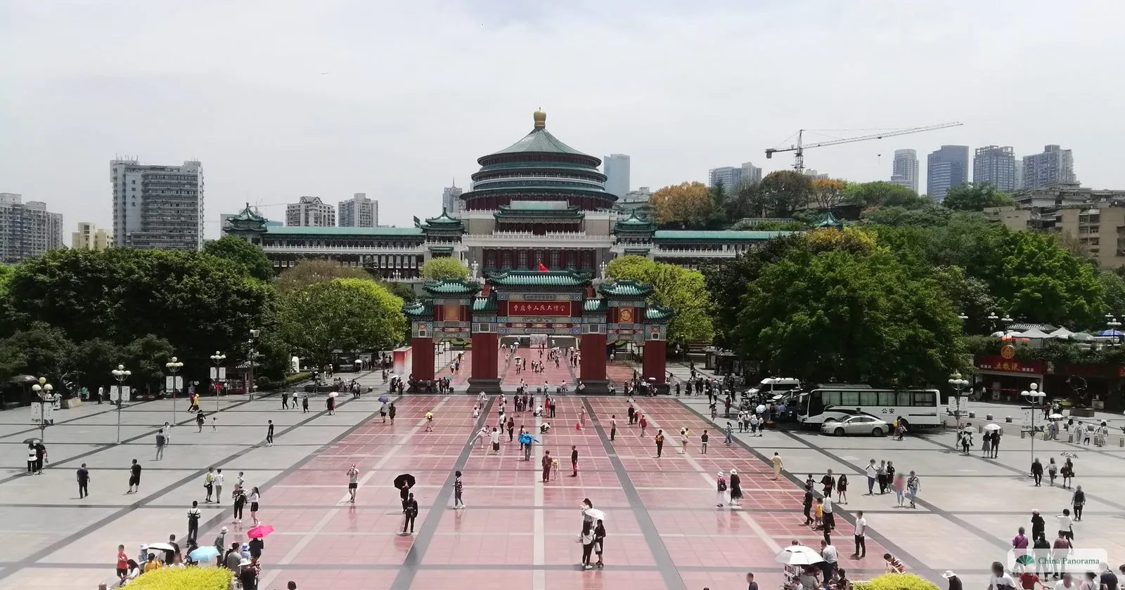 People’s Square in Chongqing from the museum steps: a long red-paved square with people walking, the red gateway and the Great Hall with its round green roof at the end