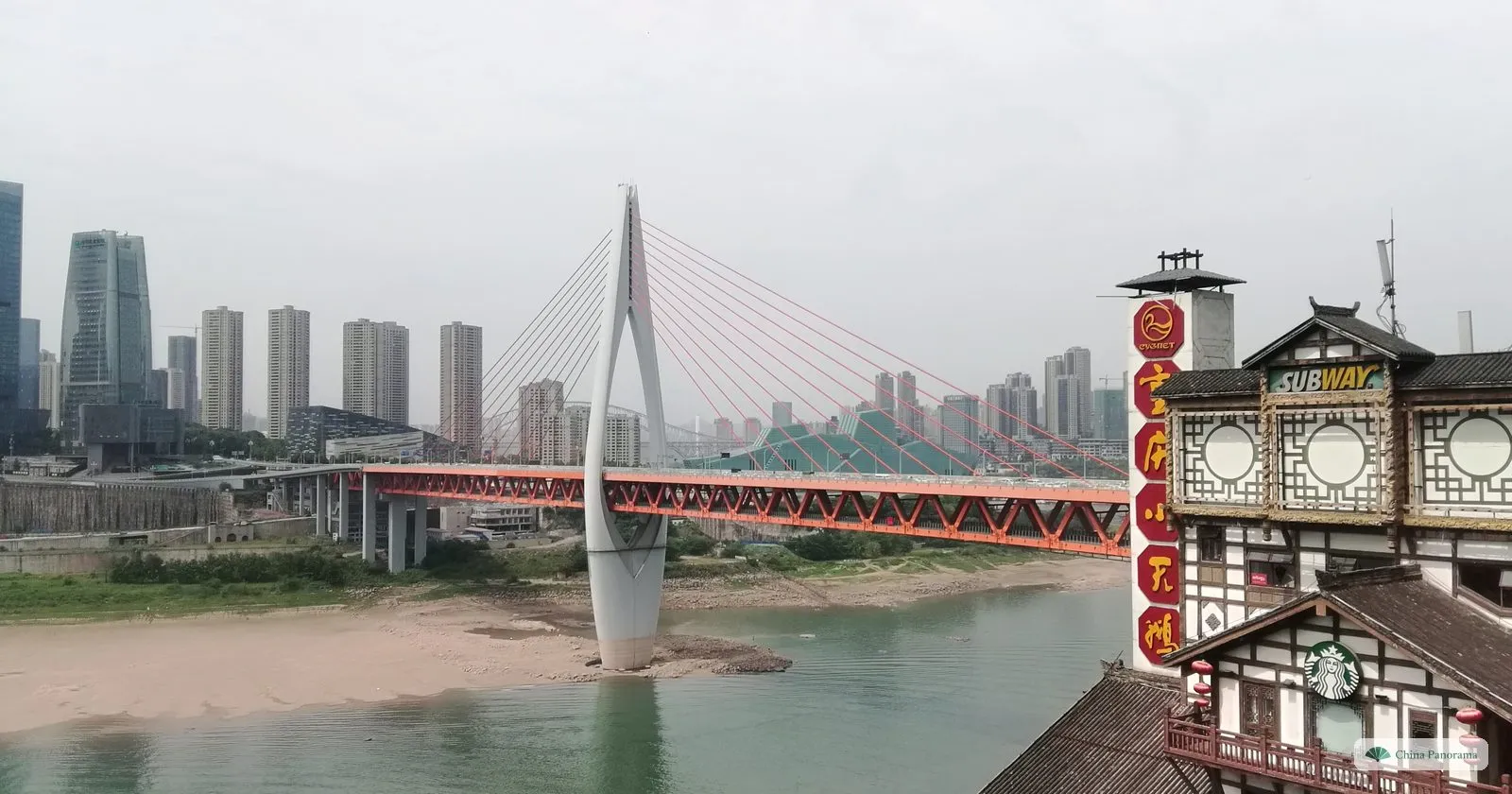 The Qiansimen Bridge by day over a low, green Jialing with sandbanks, seen from the roofs of Hongyadong with a café sign in the corner