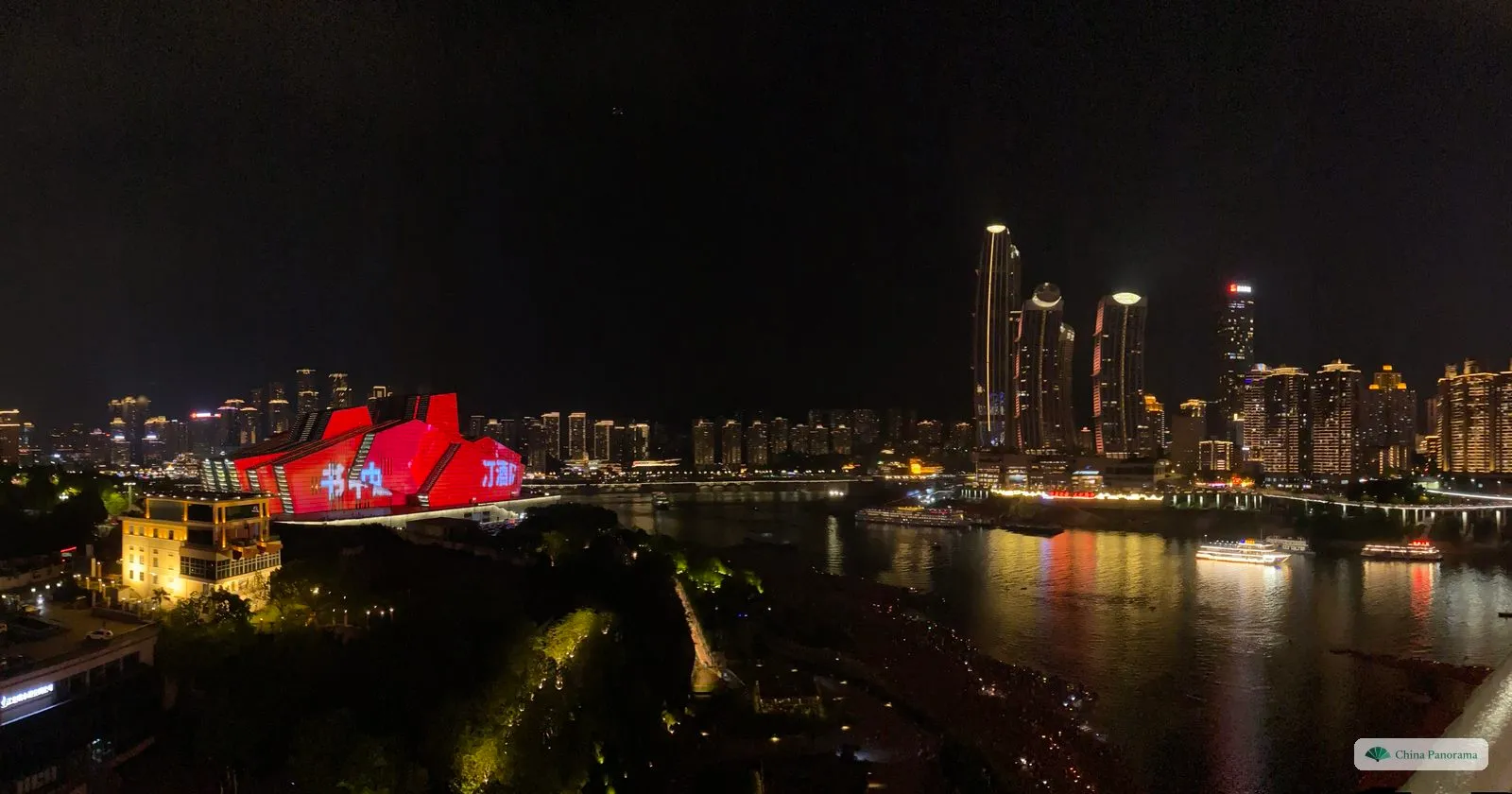 Night panorama from the footpath of the Qiansimen Bridge: a red-lit angular building on the left, the dark river, and the towers of Raffles City lit at the tip of the peninsula