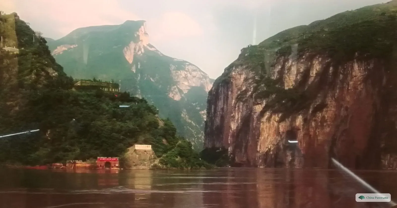 A painted panorama of one of the Three Gorges in the museum: sheer red cliffs either side of a brown river, a tunnel entrance and buildings at the water’s edge