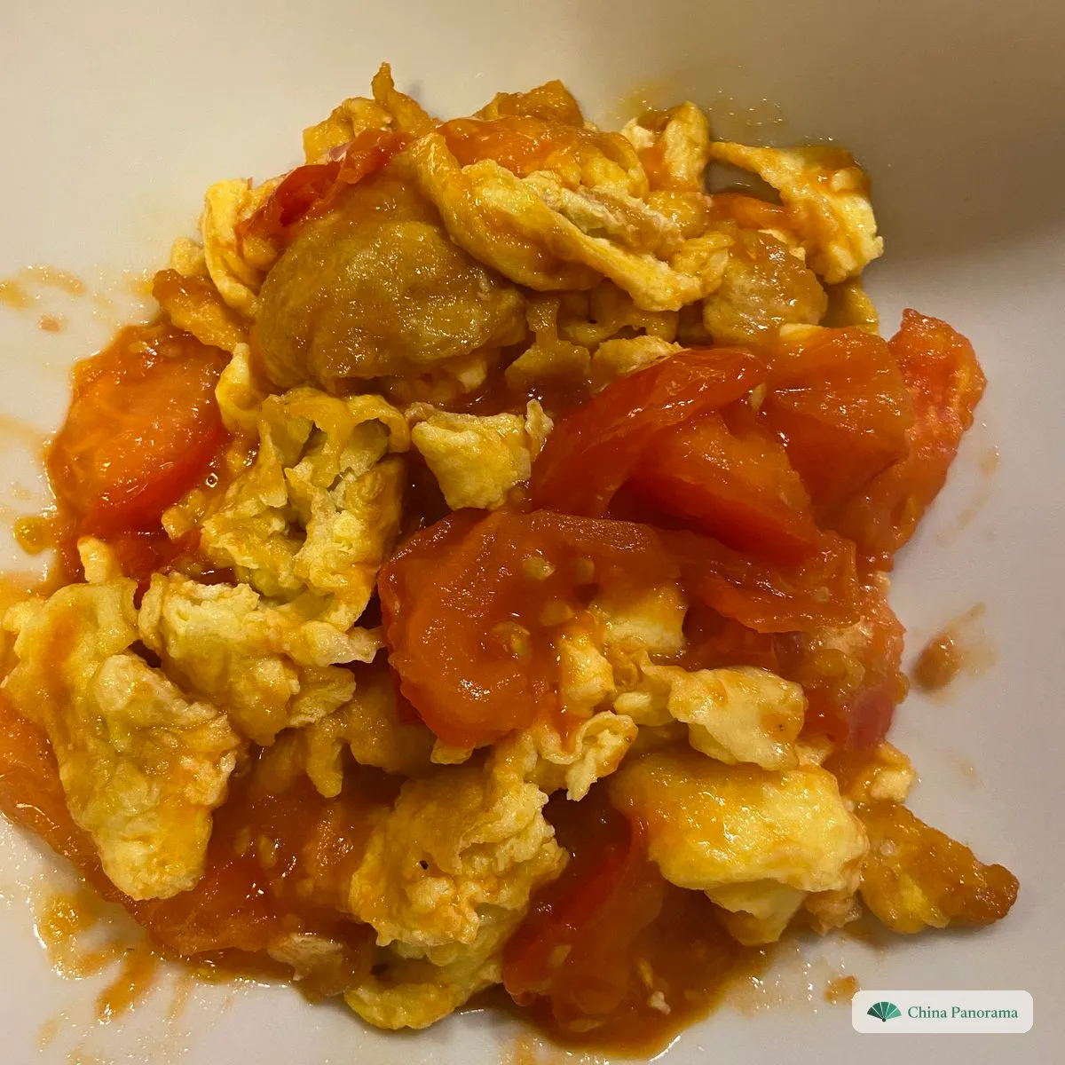 Stir-fried tomato and egg on a white plate: big, soft pieces of yellow egg and tomato wedges in a little red juice