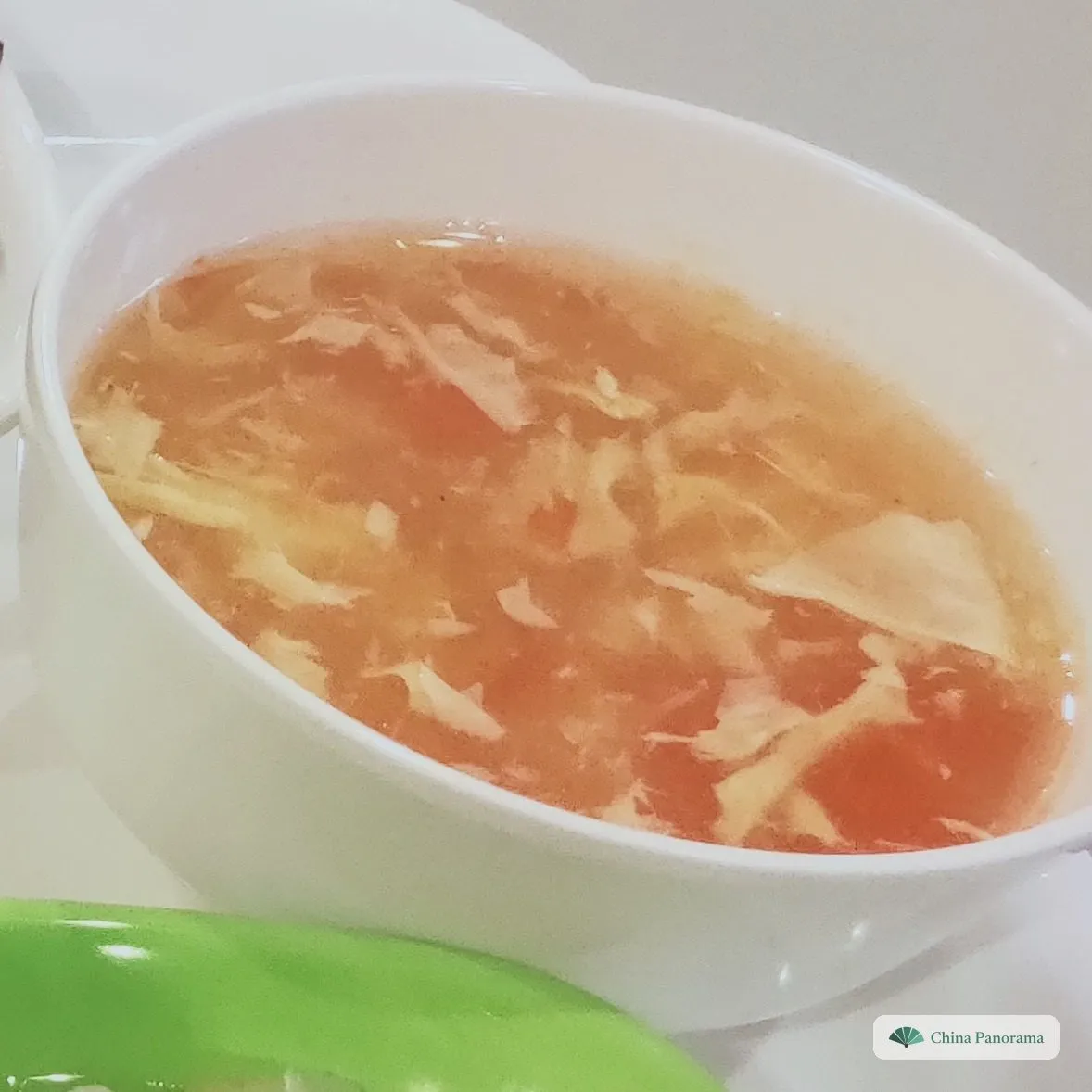A white bowl of thin orange-red soup with pale ribbons of egg floating in it