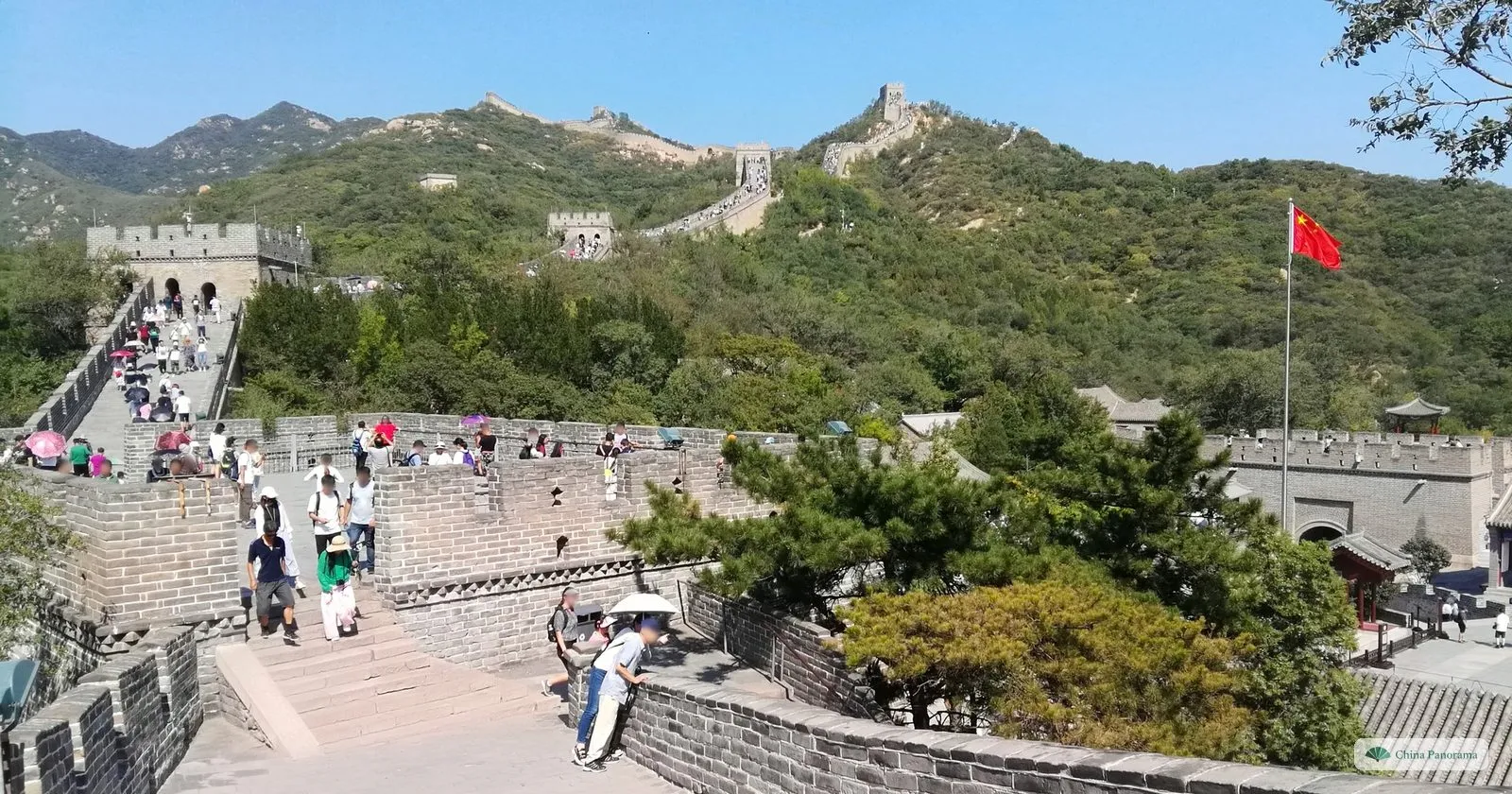 The Great Wall at Badaling on a September Saturday: visitors filling the steps up to the first watchtowers, with the wall running on over green hills and a red flag flying