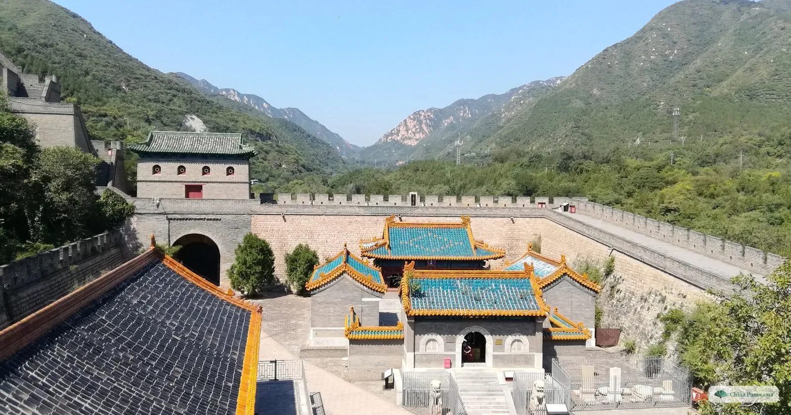 Juyongguan from the wall: a courtyard of green-roofed temple halls inside the fortress, a gate tower on the left and the wall climbing the mountains on both sides of the valley