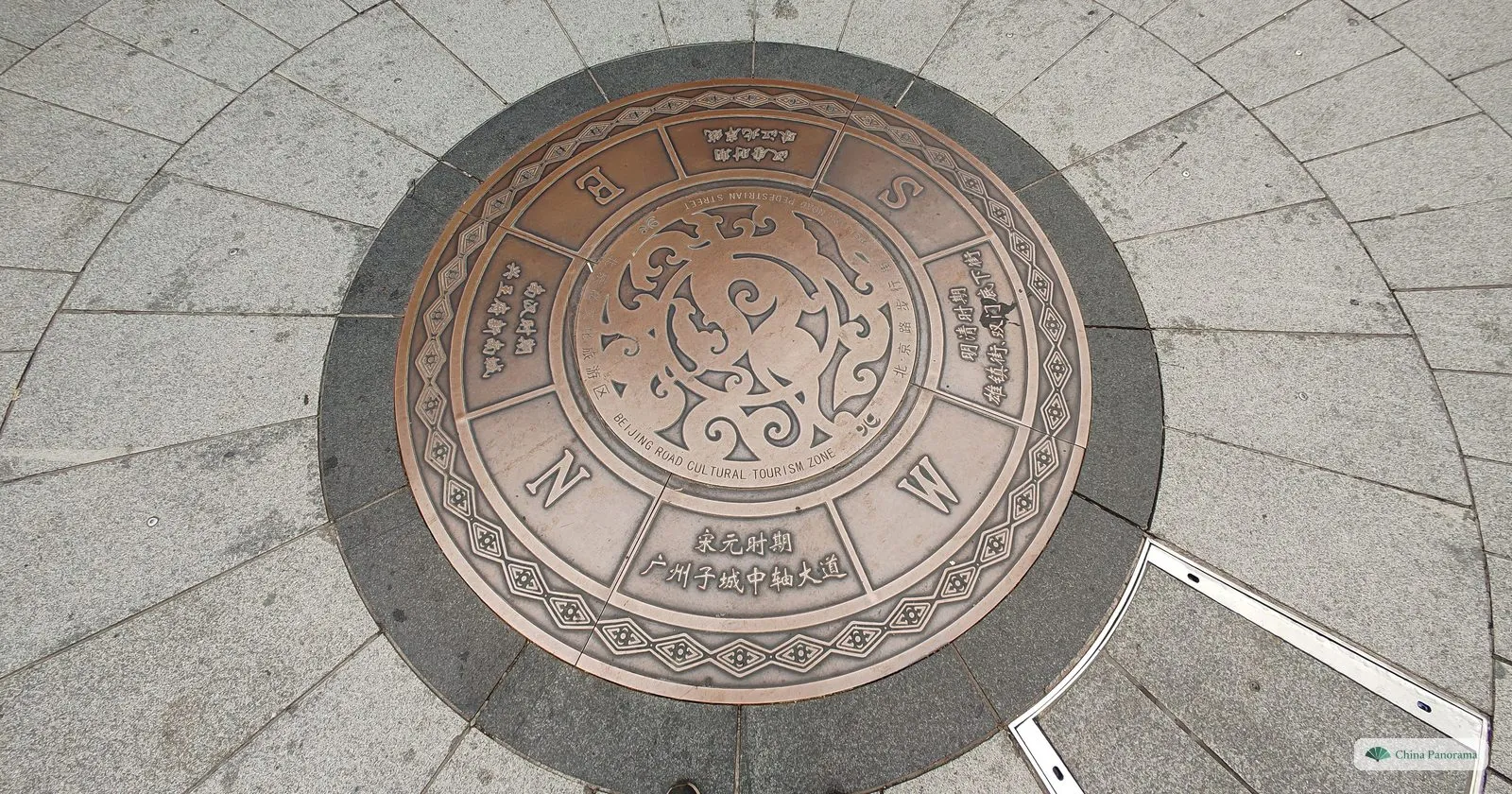 A round bronze disc set into the granite paving of Beijing Road, marked with the compass points and the inscription 宋元时期 广州子城中轴大道