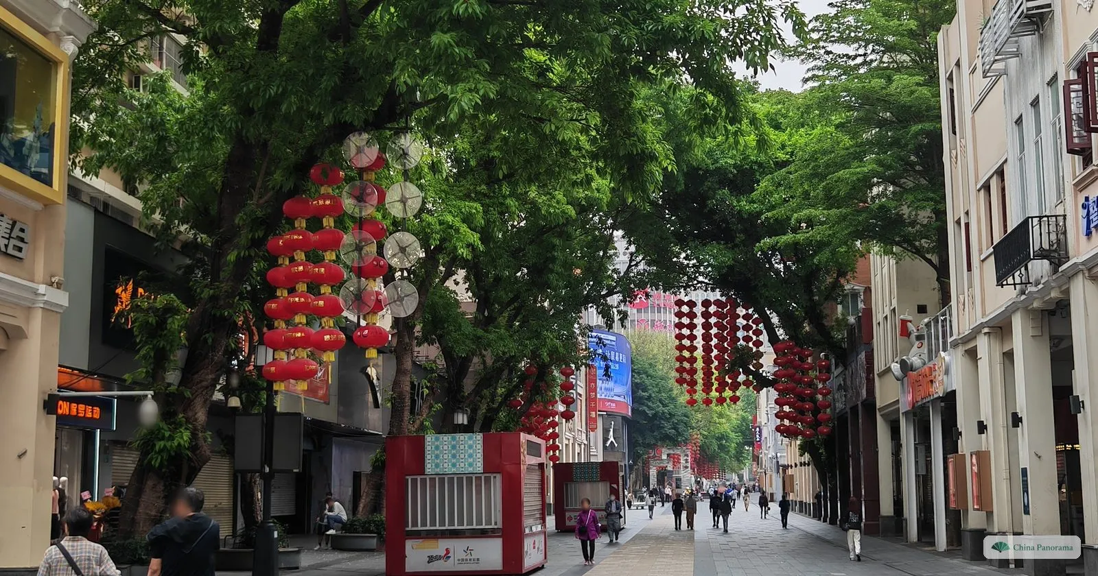 Beijing Road pedestrian street in the morning, lined with shops and trees hung with strings of red lanterns, with a few early walkers