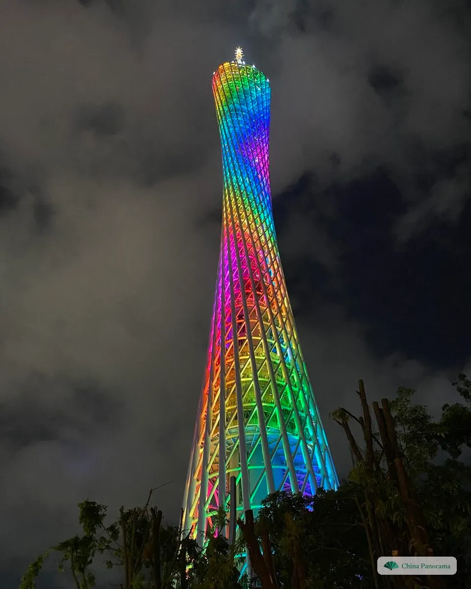 The Canton Tower from close below at night, its twisted lattice lit in rainbow colours against a cloudy sky