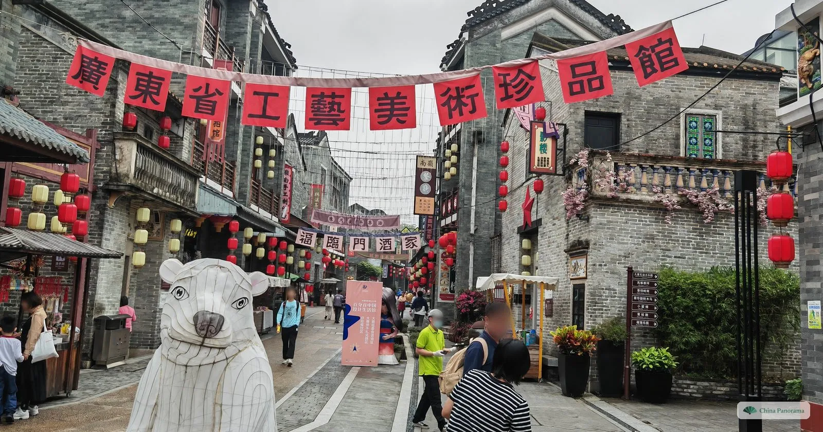 A lane of grey-brick shops in Lingnan Impression Park under a red banner reading 廣東省工藝美術珍品館, with a white bear sculpture and visitors