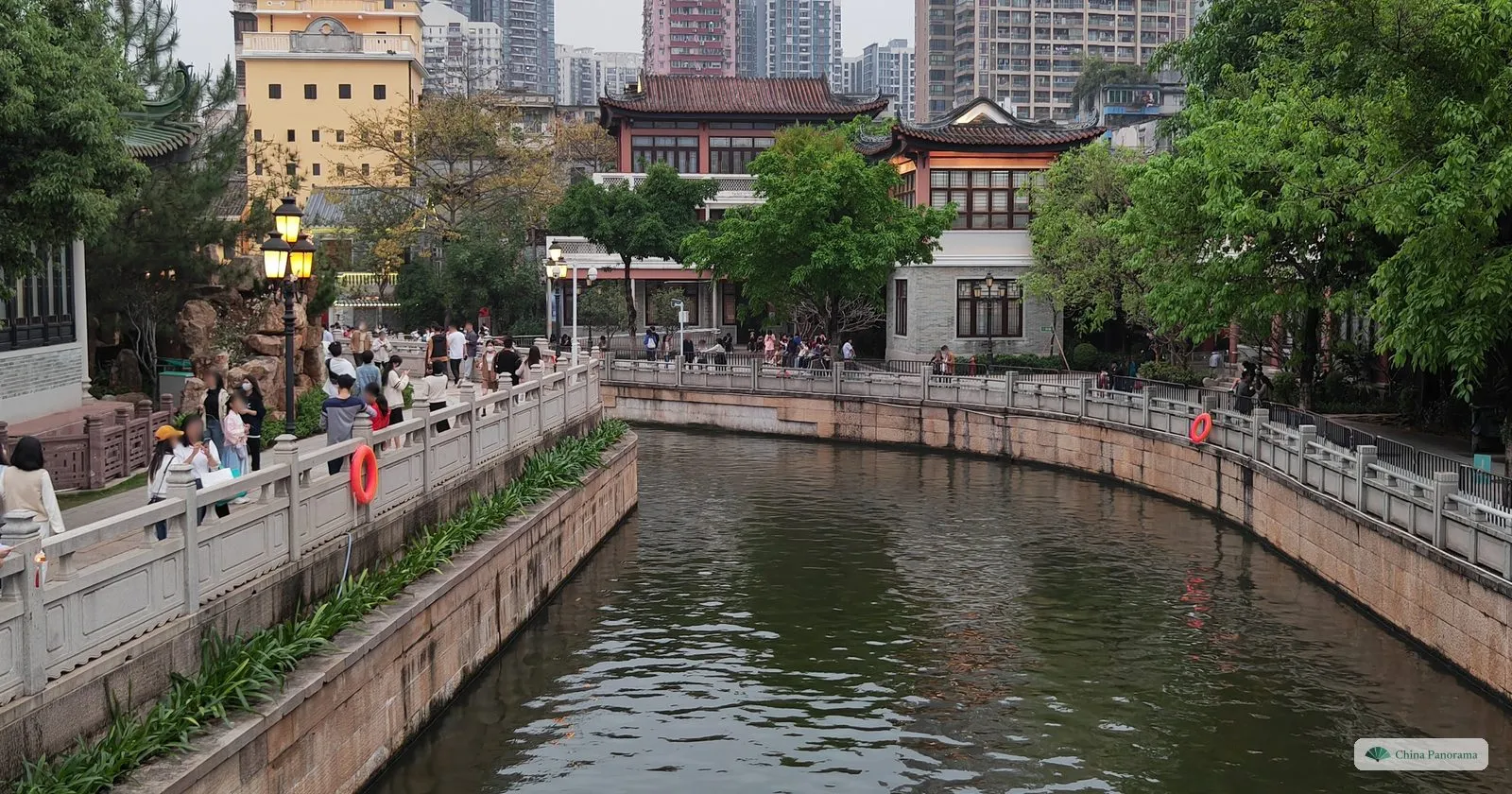 The Lizhiwan canal between stone embankments with railings, Lingnan-style halls on the far bank and people strolling along the sides