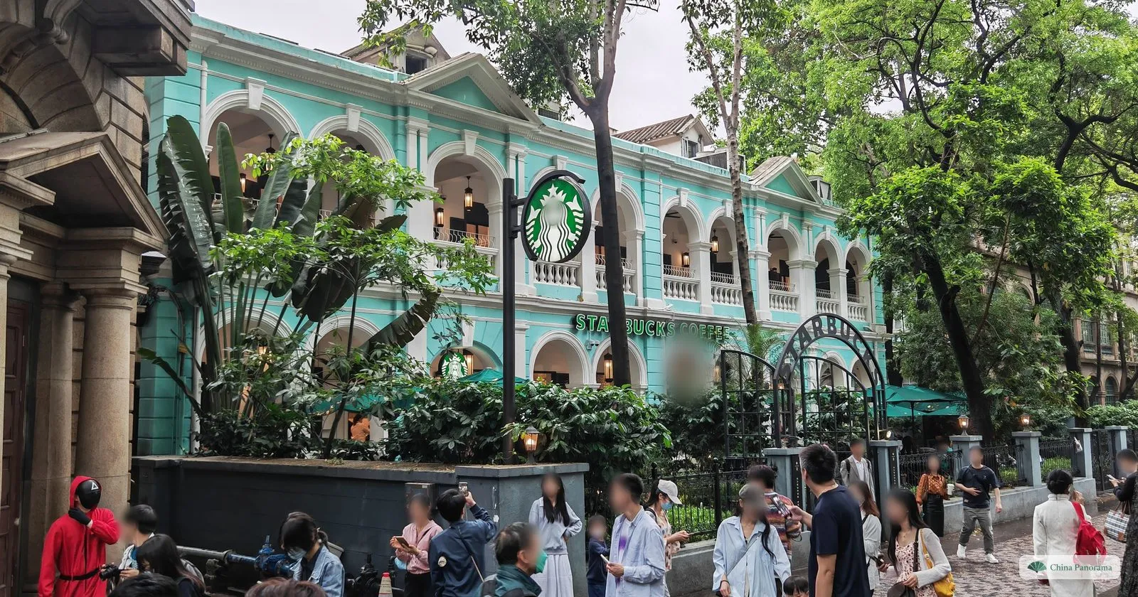 A pale green colonial building with two storeys of white arches, now a Starbucks, with a crowd of visitors on the pavement in front