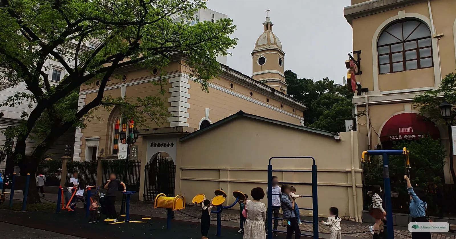 The yellow Our Lady of Lourdes Chapel on Shamian with its small domed bell tower, behind a street-side exercise area where people stretch on the equipment