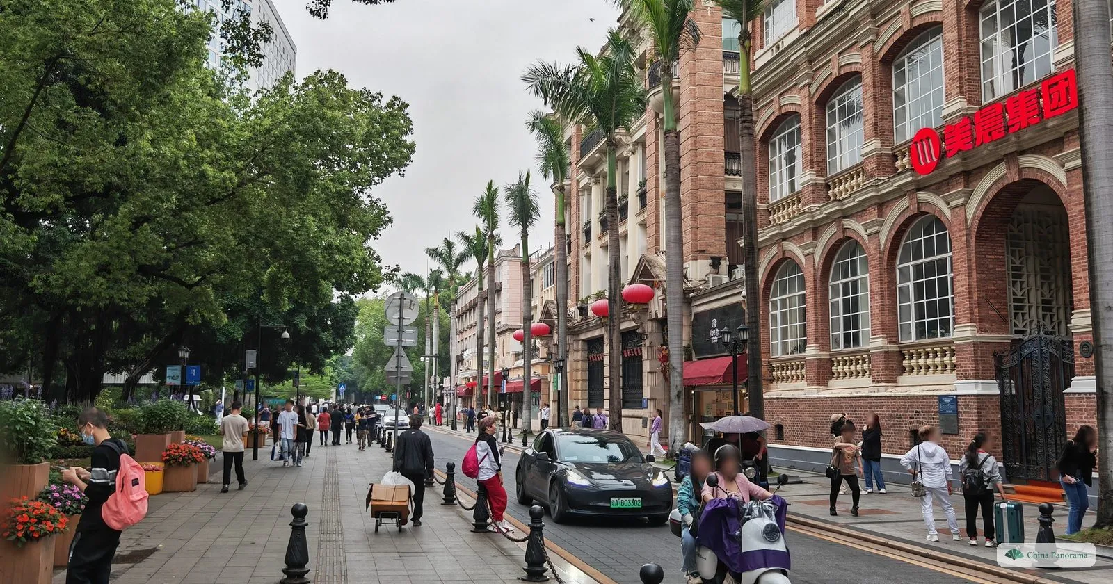 A Shamian street lined with palm trees and a red-brick colonial building with arched windows, with pedestrians and a scooter on the road