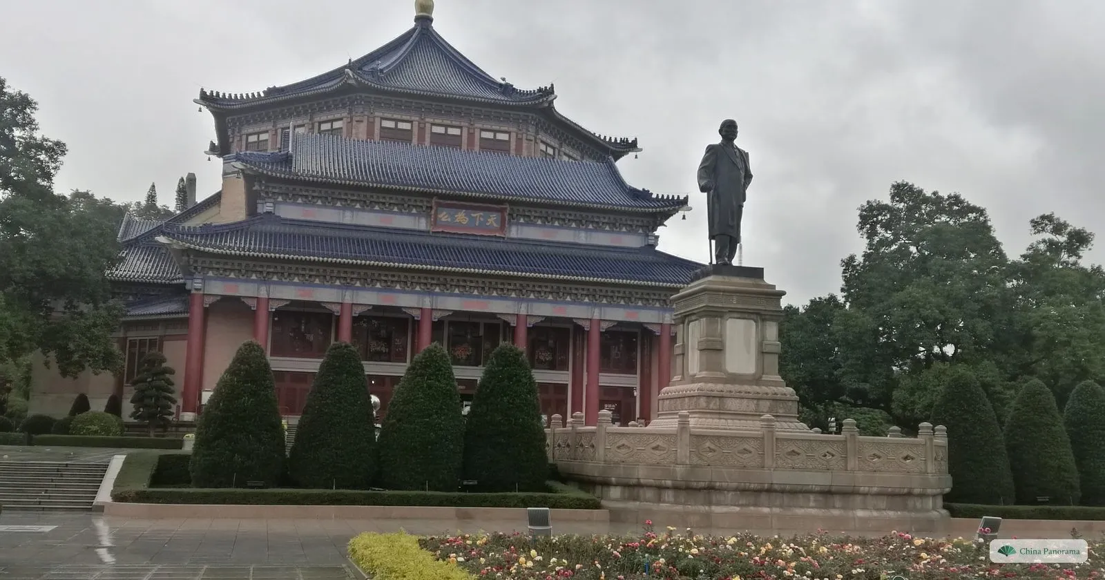 The octagonal Sun Yat-sen Memorial Hall under its blue-tiled roof on a grey, rainy day, with the bronze statue of Sun Yat-sen on a tall pedestal in front