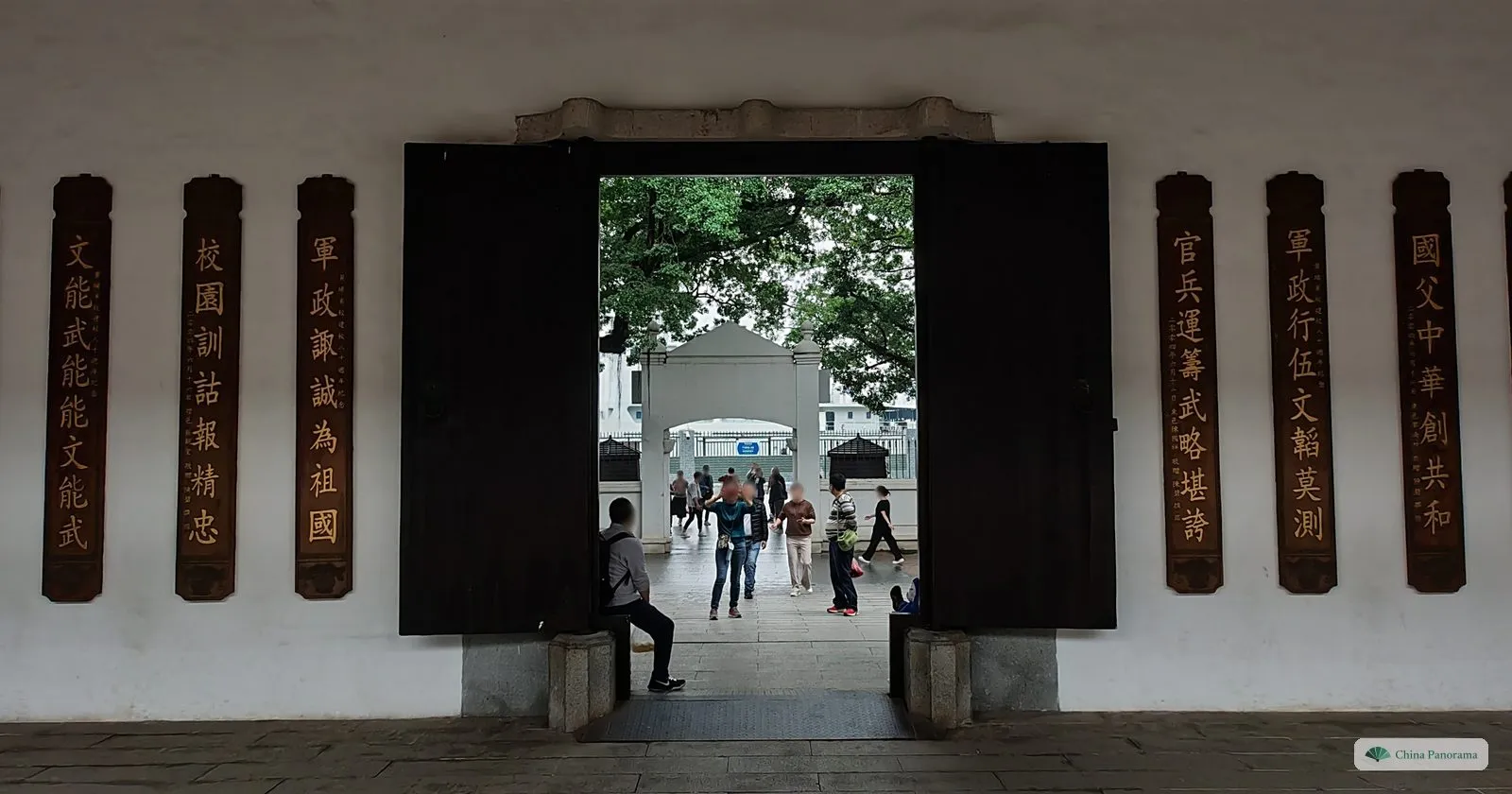 An inner door of the Whampoa academy flanked by vertical wooden boards carved with slogans, looking through to a courtyard and visitors