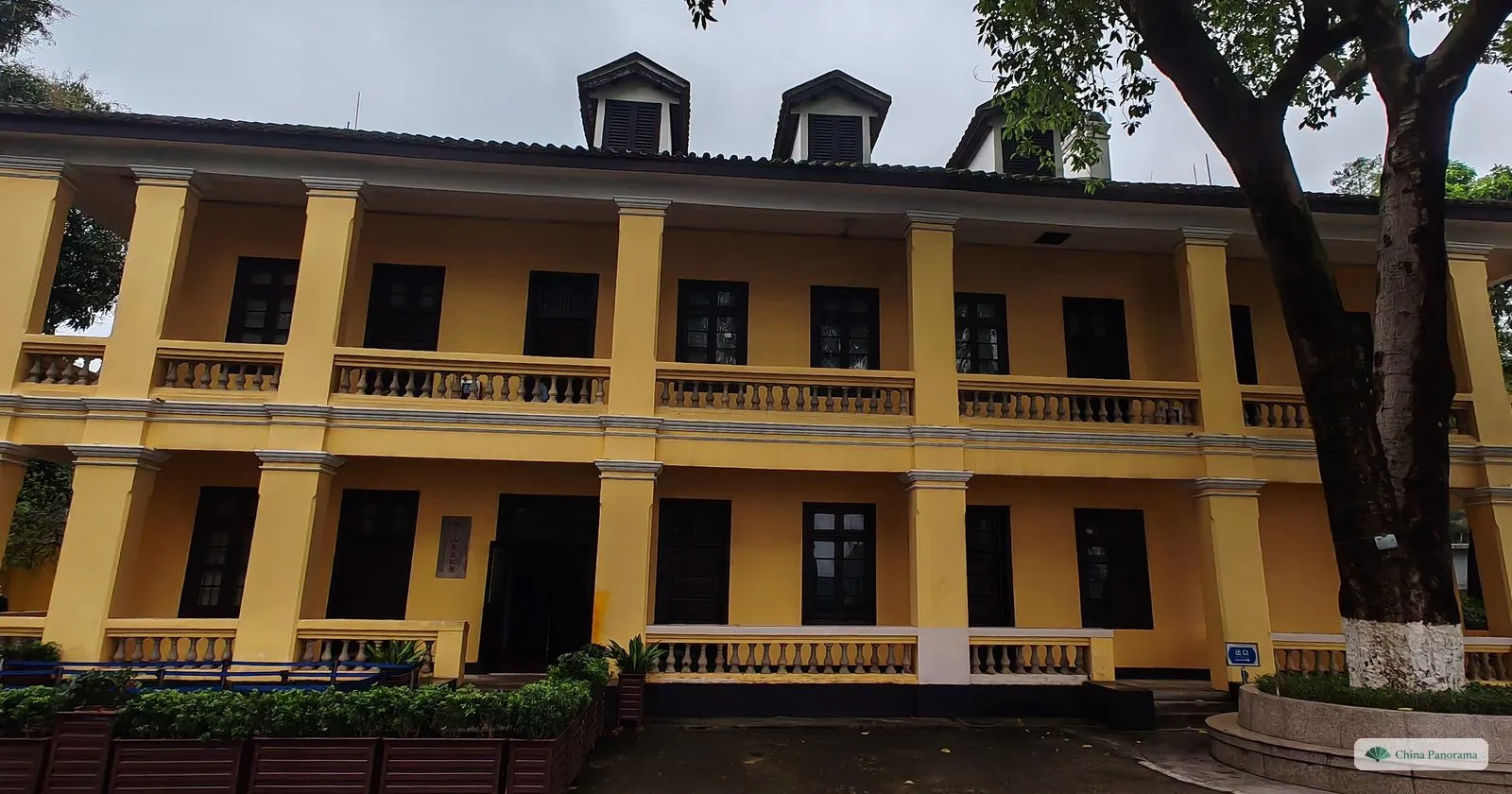 A yellow two-storey colonial-style building with columned verandas on both floors, in the grounds of the Whampoa academy