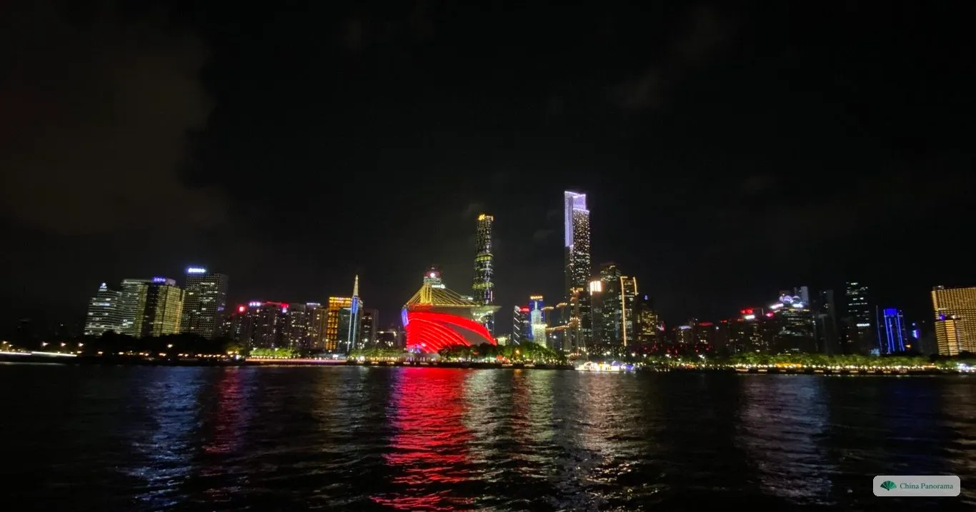 The skyline of Zhujiang New Town across the Pearl River at night: the two tallest towers lit at the top, the grandstand on Haixinsha lit red in front of them and coloured reflections in the water