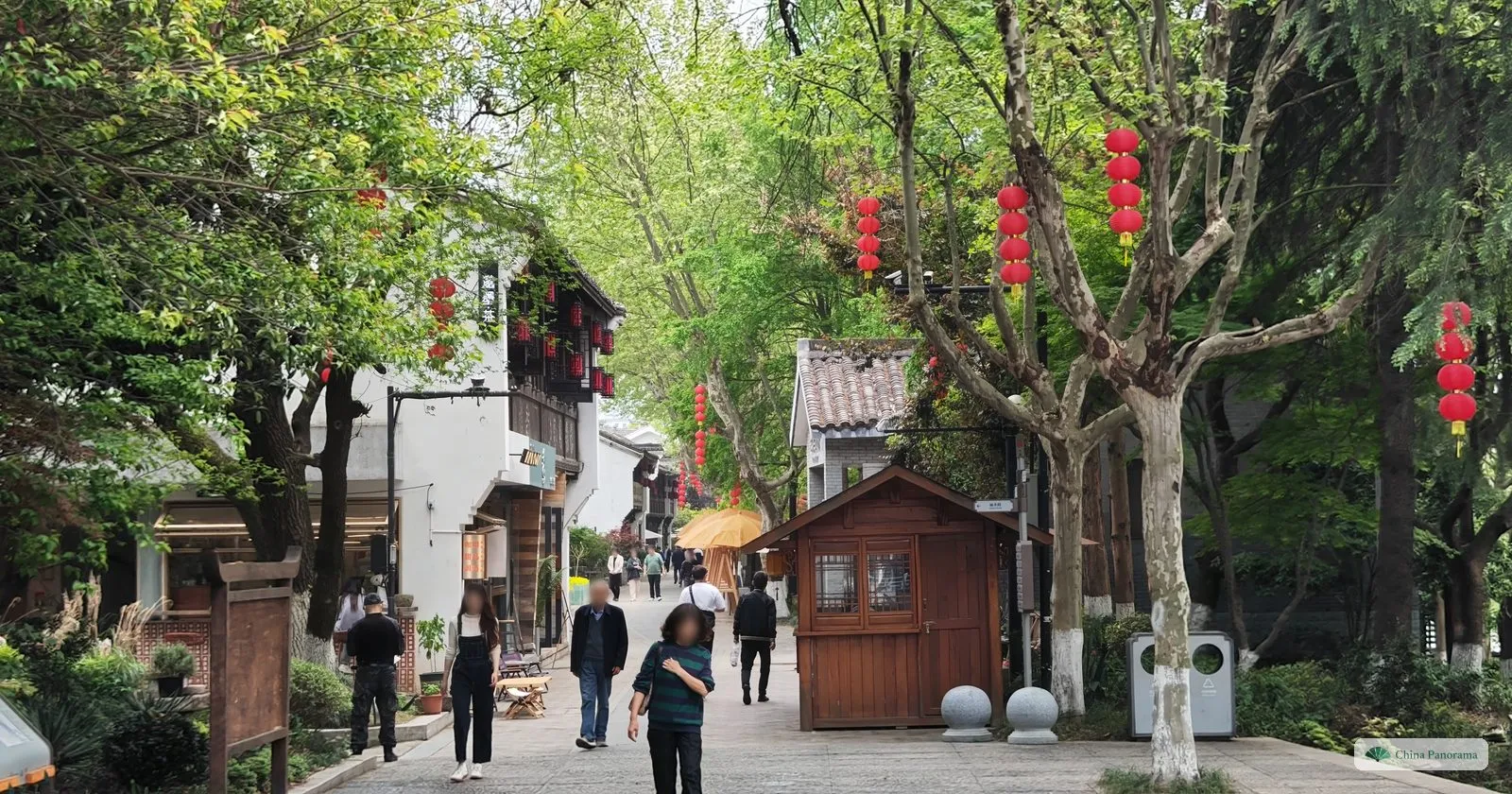 A paved street of white houses with red lanterns in the trees and a small wooden kiosk