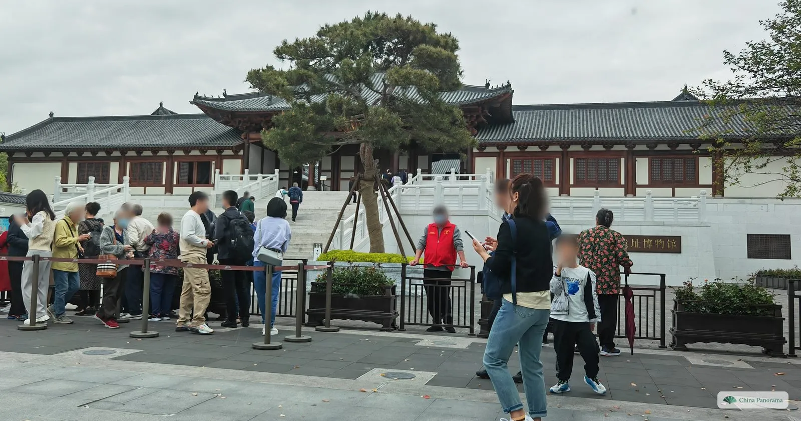 A queue of visitors behind barriers in front of a Song-style hall on a white stone terrace