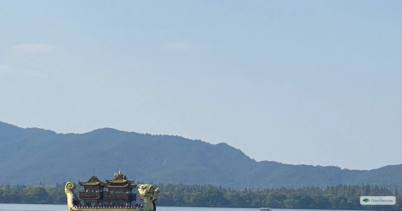 A golden dragon-headed pleasure boat on a calm lake below a long line of hills