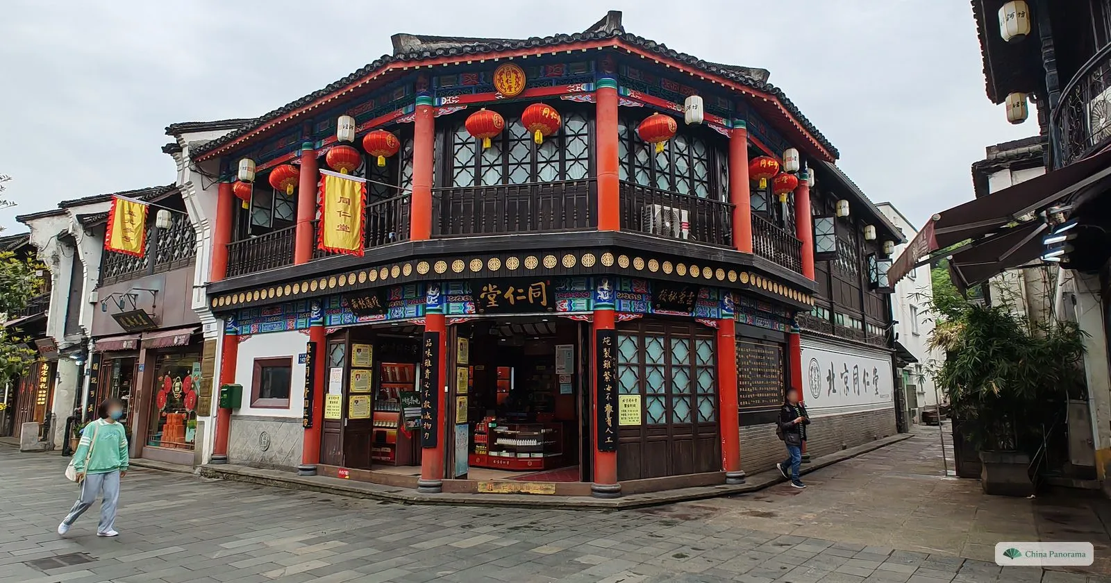An ornate two-storey corner shop with red columns, red lanterns and dark wooden windows on a paved street